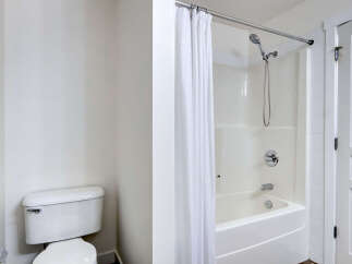 This bathroom features a pristine white toilet and a modern shower/tub combination with a sleek chrome showerhead and faucet.