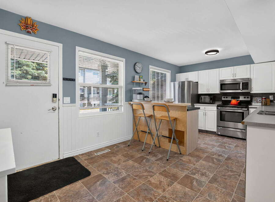 This charming kitchen features white cabinetry, stainless steel appliances, and a convenient breakfast bar with seating.