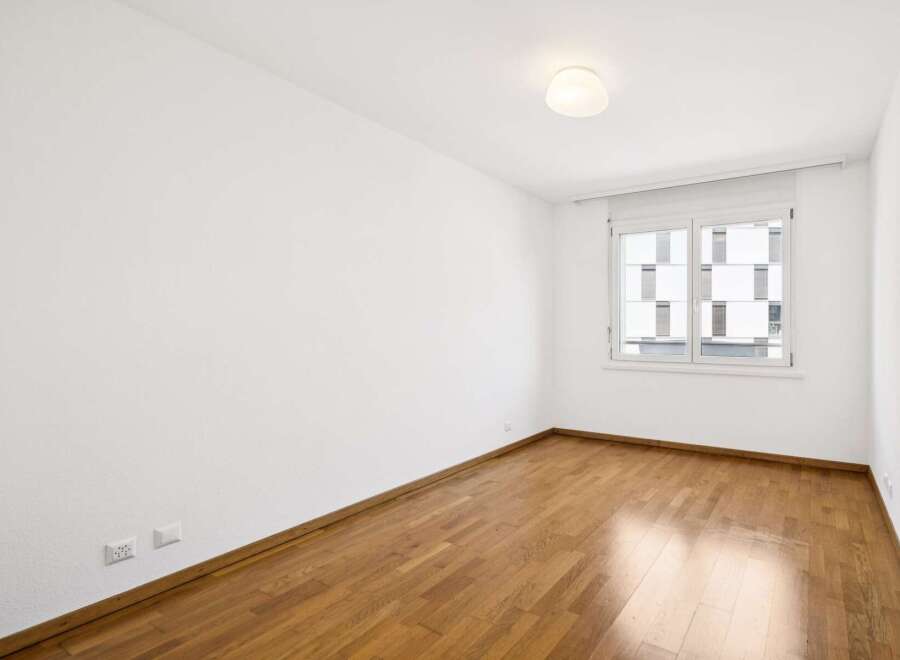 This empty room features a beautiful hardwood floor that gleams under the natural light streaming in from the large window.