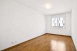 This empty room features a beautiful hardwood floor that gleams under the natural light streaming in from the large window.