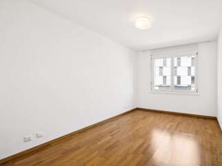 This empty room features a beautiful hardwood floor that gleams under the natural light streaming in from the large window.