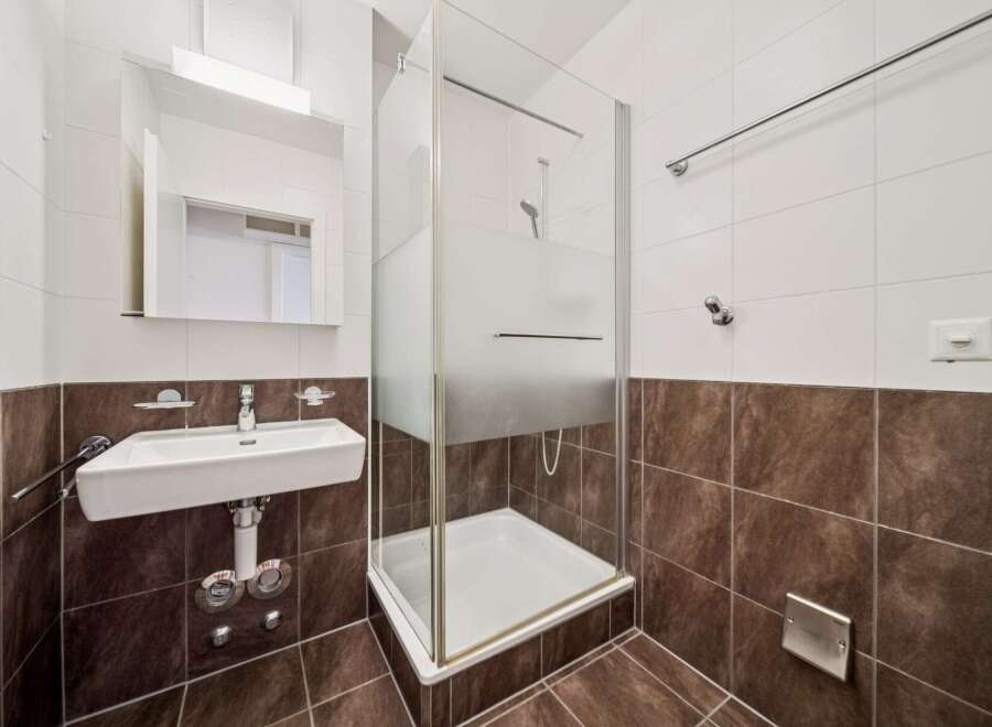 This modern bathroom features a sleek white sink with chrome fixtures, complemented by a frosted glass shower enclosure.