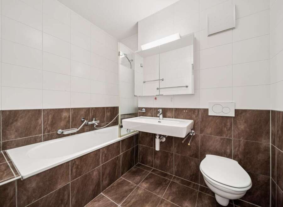 This modern bathroom features a sleek white bathtub with a glass shower screen, complemented by a wall-mounted sink and a modern toilet.