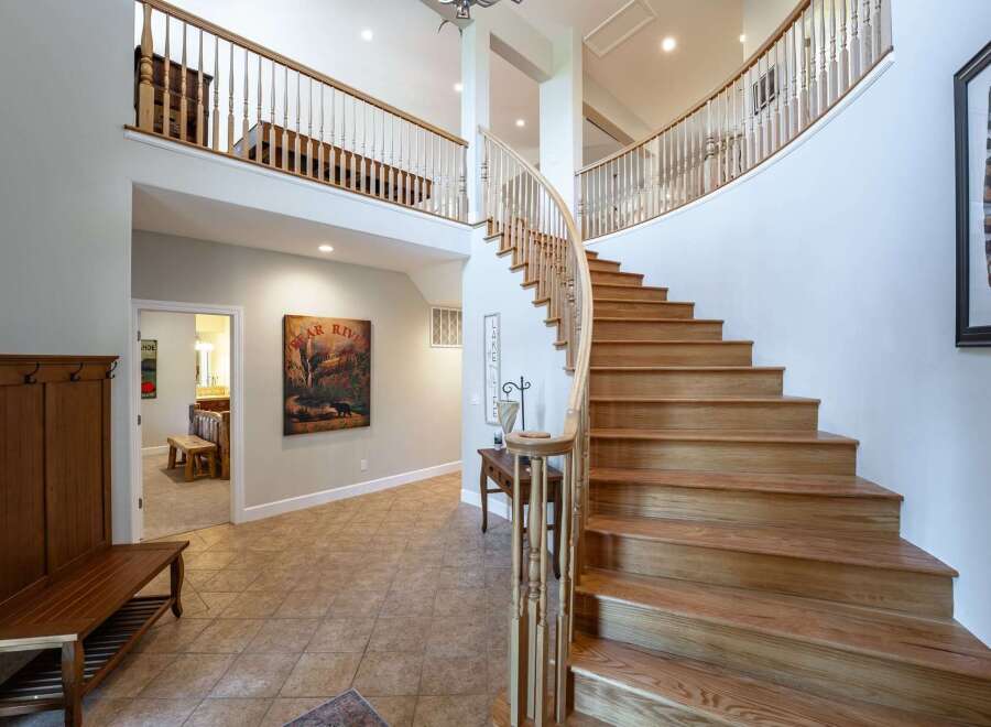 This grand foyer boasts a stunning curved staircase with natural wood treads and a white balustrade, leading to a spacious upper landing.