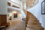 This grand foyer boasts a stunning curved staircase with natural wood treads and a white balustrade, leading to a spacious upper landing.