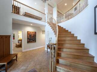 This grand foyer boasts a stunning curved staircase with natural wood treads and a white balustrade, leading to a spacious upper landing.