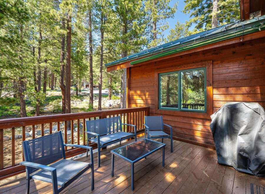 Enjoy the serene mountain setting from this charming cabin's wooden deck, complete with comfortable seating and a grill for outdoor cooking.