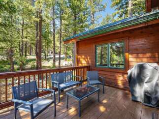 Enjoy the serene mountain setting from this charming cabin's wooden deck, complete with comfortable seating and a grill for outdoor cooking.