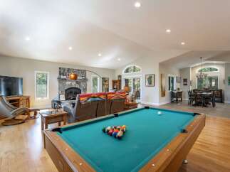 Experience ultimate relaxation and entertainment in this spacious open-concept living area, featuring a cozy stone fireplace and a dedicated game room with a pool table.