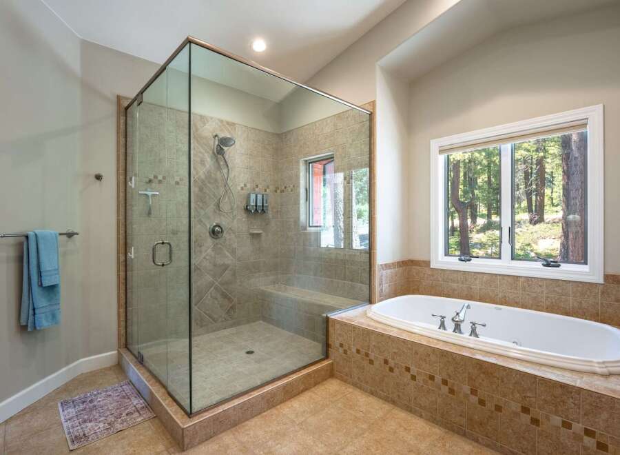 Experience luxury in this spacious bathroom, featuring a stunning glass-enclosed walk-in shower with multiple showerheads and a built-in bench.