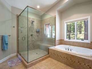 Experience luxury in this spacious bathroom, featuring a stunning glass-enclosed walk-in shower with multiple showerheads and a built-in bench.