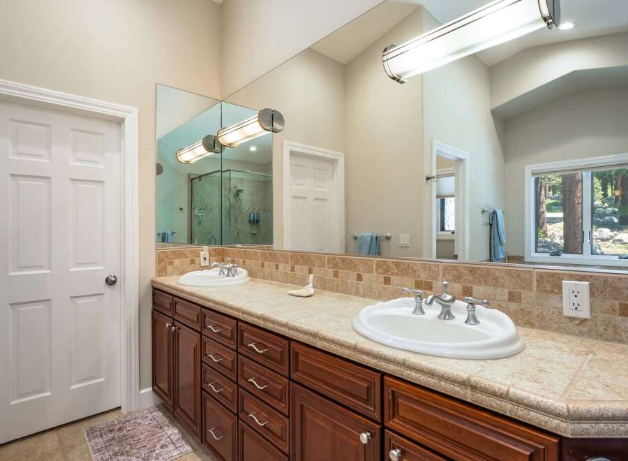 This spacious bathroom features a double vanity with elegant wood cabinetry and a tiled backsplash.