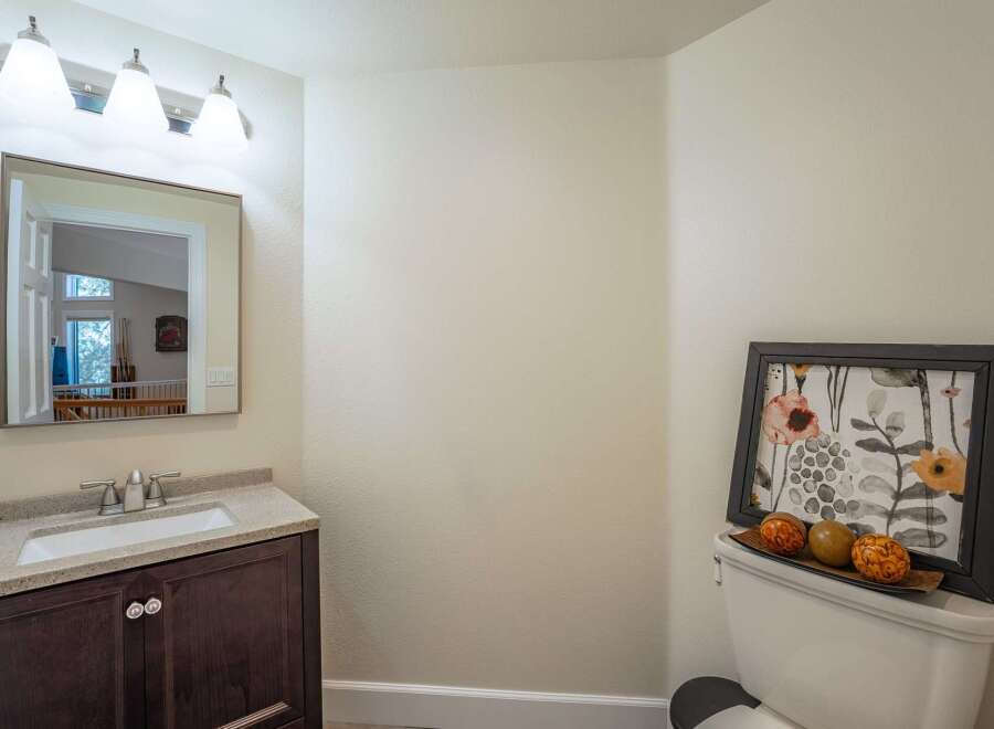 This bathroom features a modern vanity with a granite countertop and a sleek faucet, complemented by a large vanity mirror with an attached light fixture.