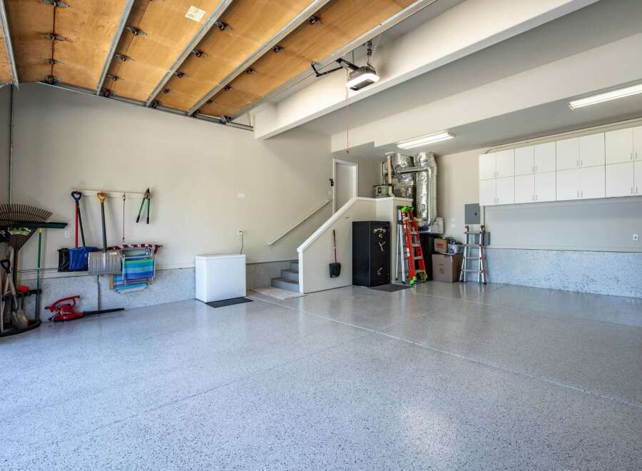 Discover ample storage and organization in this spacious garage, featuring a wall of white cabinets and a durable, speckled epoxy floor.