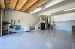 Discover ample storage and organization in this spacious garage, featuring a wall of white cabinets and a durable, speckled epoxy floor.