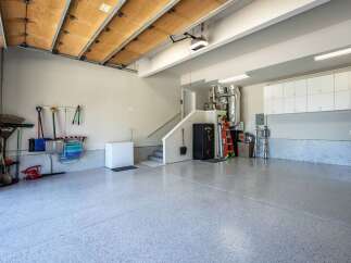 Discover ample storage and organization in this spacious garage, featuring a wall of white cabinets and a durable, speckled epoxy floor.