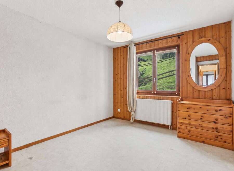 Experience rustic charm in this inviting bedroom, featuring warm wood paneling and a large window with scenic mountain views.