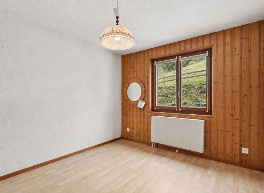 Experience rustic charm in this cozy room featuring warm wood-paneled walls and a large window offering picturesque views of a green hillside.