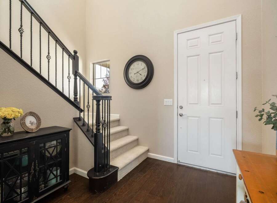 Step into this inviting entryway featuring a grand staircase with elegant black railings and a charming console table adorned with a vase of yellow roses and a decorative picture frame.