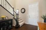 Step into this inviting entryway featuring a grand staircase with elegant black railings and a charming console table adorned with a vase of yellow roses and a decorative picture frame.