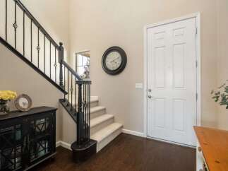 Step into this inviting entryway featuring a grand staircase with elegant black railings and a charming console table adorned with a vase of yellow roses and a decorative picture frame.