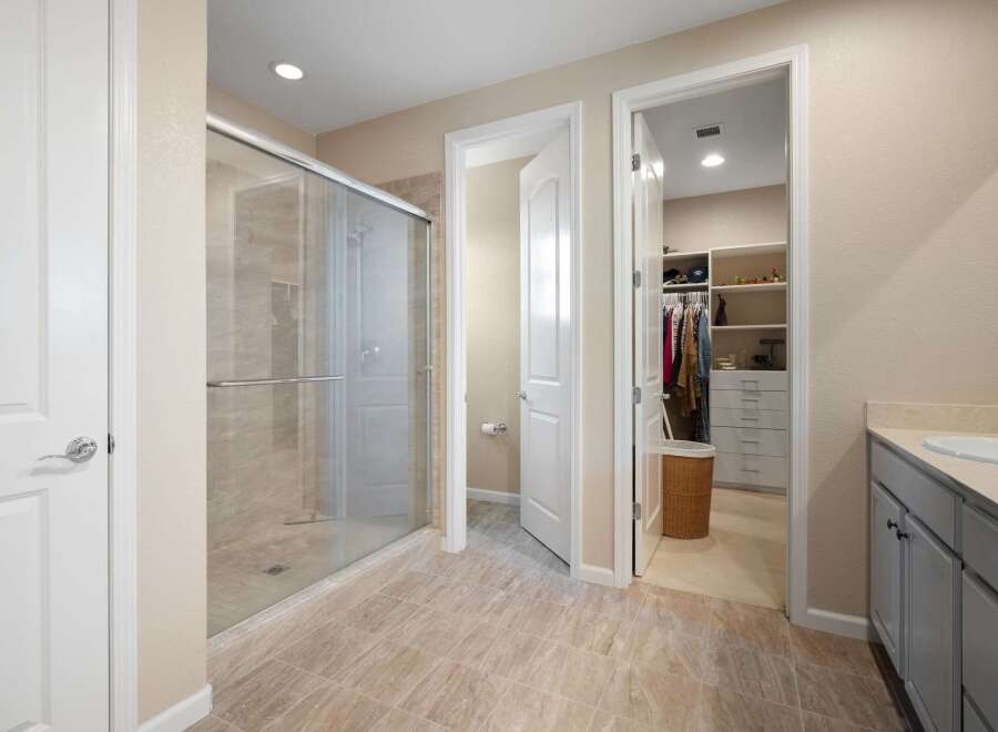 Step into this luxurious master bathroom featuring a spacious glass-enclosed shower and a walk-in closet with ample storage.