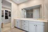This spacious master bathroom features a double vanity with ample counter space and storage, complemented by a large mirror reflecting the adjacent walk-in closet.
