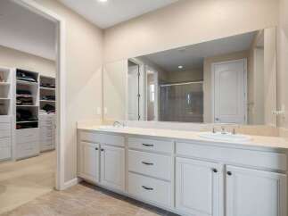 This spacious master bathroom features a double vanity with ample counter space and storage, complemented by a large mirror reflecting the adjacent walk-in closet.