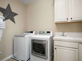 This laundry room features a stacked washer and dryer set, a utility sink, and ample cabinet storage.