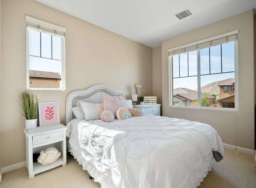 This charming bedroom features a cozy white wicker bed adorned with plush pillows and a playful rainbow accent.