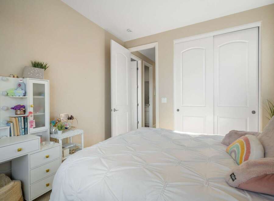 This charming bedroom features a spacious white comforter on a bed, complemented by a white vanity with drawers and a mirrored cabinet.