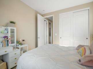 This charming bedroom features a spacious white comforter on a bed, complemented by a white vanity with drawers and a mirrored cabinet.