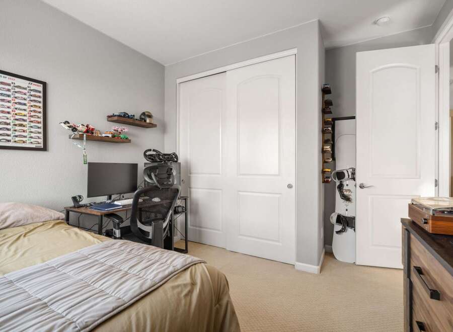 This bedroom features a comfortable bed, a dedicated gaming or study area with a computer and racing wheel, and ample storage solutions including a large closet and shelves displaying collectibles.