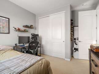 This bedroom features a comfortable bed, a dedicated gaming or study area with a computer and racing wheel, and ample storage solutions including a large closet and shelves displaying collectibles.