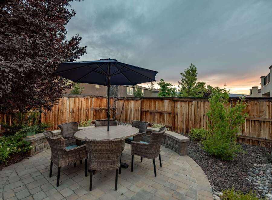 Enjoy outdoor living in this charming backyard featuring a paved patio with a dining set and umbrella, perfect for al fresco meals.
