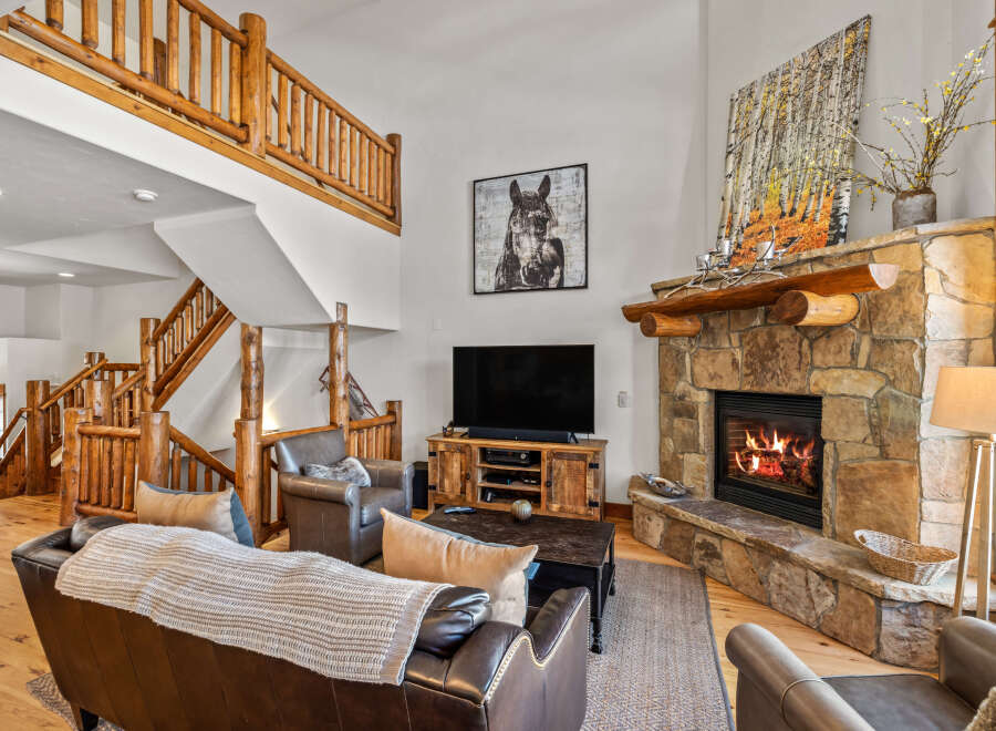 Experience rustic charm in this spacious living room, featuring a grand stone fireplace and a beautiful log-accented staircase.