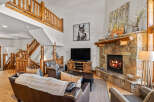 Experience rustic charm in this spacious living room, featuring a grand stone fireplace and a beautiful log-accented staircase.