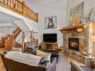 Experience rustic charm in this spacious living room, featuring a grand stone fireplace and a beautiful log-accented staircase.