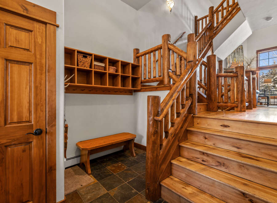 Experience rustic charm with this stunning log staircase and entryway, featuring a convenient wooden bench and ample shelving for storage.