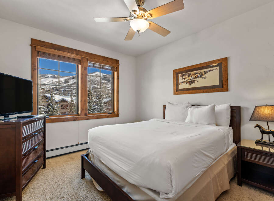 Experience breathtaking mountain views from this cozy bedroom, featuring a comfortable queen-size bed and a large window overlooking a snowy landscape.