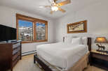 Experience breathtaking mountain views from this cozy bedroom, featuring a comfortable queen-size bed and a large window overlooking a snowy landscape.