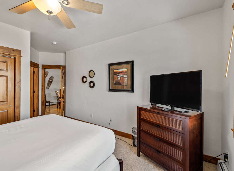 This charming bedroom features a comfortable bed, a modern flat-screen TV, and ample storage with a wooden dresser.