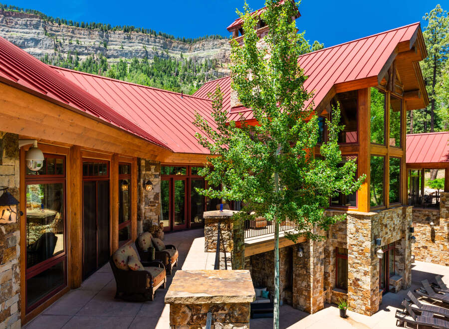 Experience luxury mountain living in this stunning stone and timber home, featuring a vibrant red metal roof and expansive windows that capture breathtaking natural views.