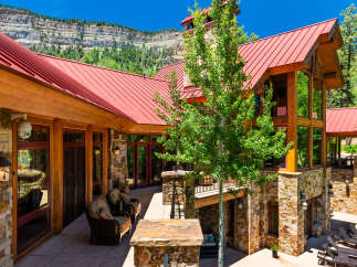 Experience luxury mountain living in this stunning stone and timber home, featuring a vibrant red metal roof and expansive windows that capture breathtaking natural views.