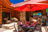 Enjoy al fresco dining on this stunning mountain property with a spacious outdoor patio, complete with a large dining table set for guests and a vibrant red umbrella for shade.