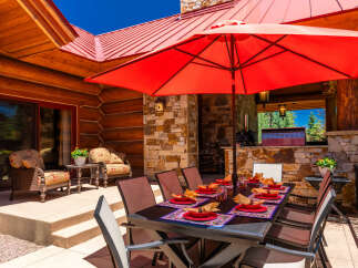 Enjoy al fresco dining on this stunning mountain property with a spacious outdoor patio, complete with a large dining table set for guests and a vibrant red umbrella for shade.