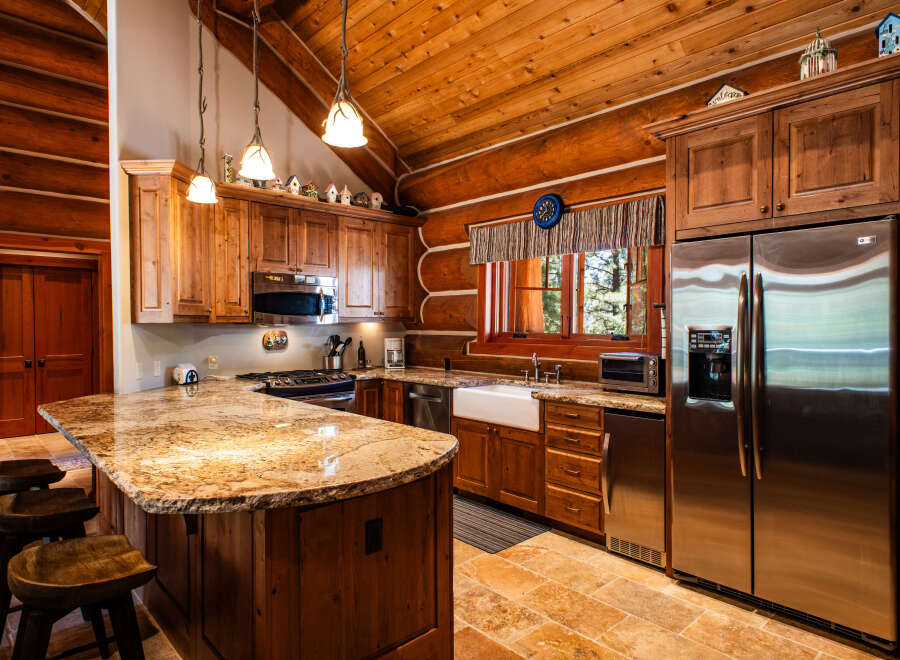 Experience rustic charm in this log cabin kitchen, featuring a spacious granite island with bar seating and custom wood cabinetry.