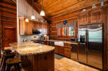 Experience rustic charm in this log cabin kitchen, featuring a spacious granite island with bar seating and custom wood cabinetry.