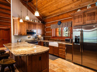 Experience rustic charm in this log cabin kitchen, featuring a spacious granite island with bar seating and custom wood cabinetry.