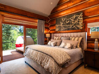 Experience rustic luxury in this stunning log cabin bedroom, featuring a plush king-sized bed adorned with decorative pillows and a cozy comforter.